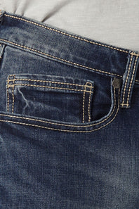 Close-up of dark blue denim jeans showing the back pocket with contrast tan stitching, a metal button, and a light gray top fabric at the waist.