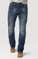 A person wearing blue denim jeans with a faded wash, paired with tan boots and a light gray shirt, shown from the waist down on a plain light gray studio background.