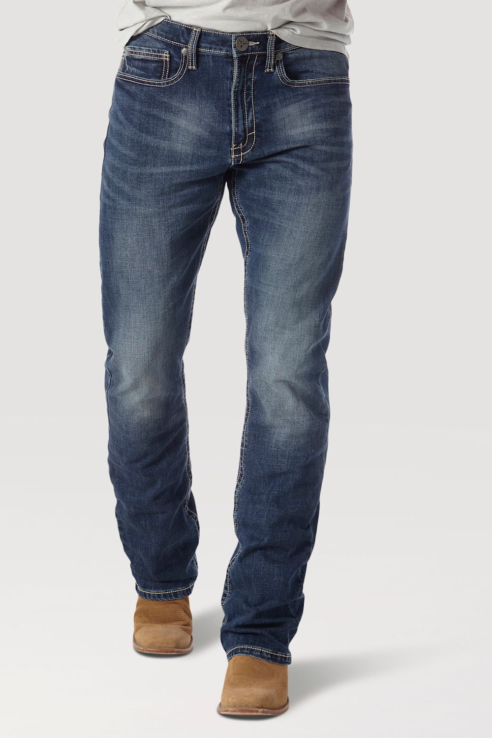 A person wearing blue denim jeans with a faded wash, paired with tan boots and a light gray shirt, shown from the waist down on a plain light gray studio background.