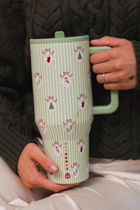 A person holding a HydroJug travel tumbler with a light green and white striped pattern decorated with small holiday motifs, wearing a dark cable-knit sweater.
