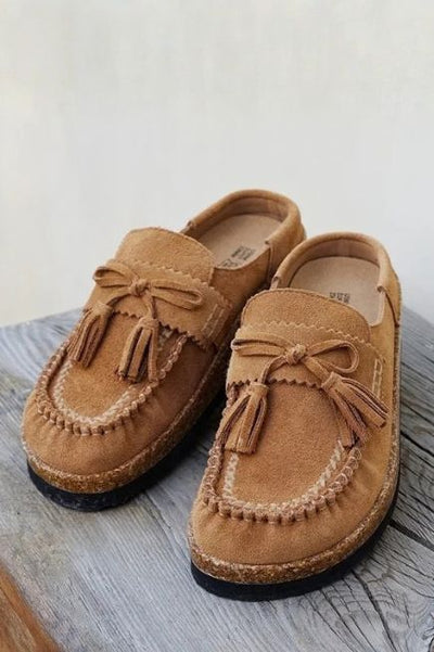 A pair of Moccasin style mules on top of a wood board