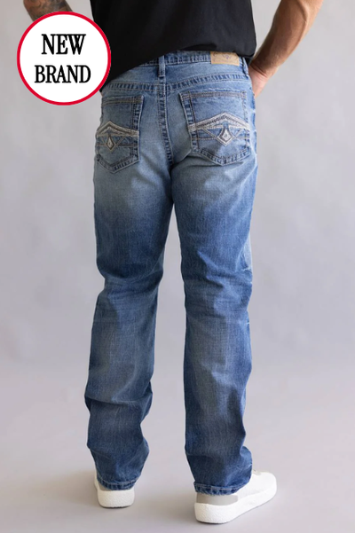 Man wearing blue jeans and white sneakers stands against a gray background. Jeans have embroidered back pockets. 