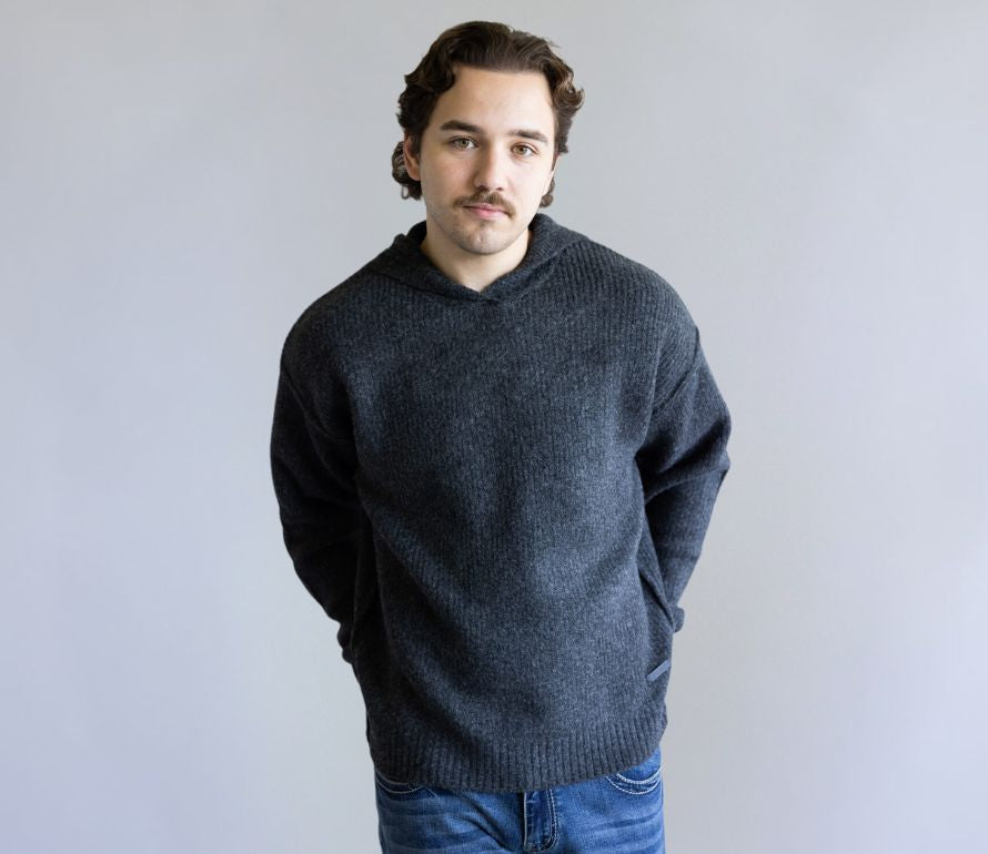 Man wearing a dark gray sweater and blue jeans against a plain background