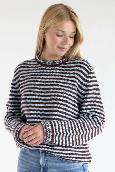 Woman wearing a brown and blue striped sweater with denim jeans standing in front of a plain studio background