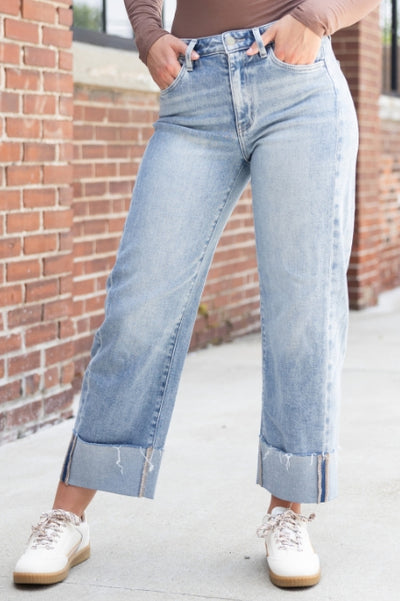 Woman viewed from the waist down standing in front of a brick wall wearing light wash denim jeans with a brown top and white sneakers