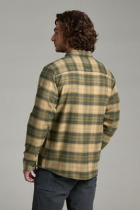 A man wearing a beige and green plaid flannel shirt, shown from the back against a solid gray studio background.