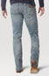 Rear view of a person wearing light-wash blue denim jeans with brown leather boots and a dark navy long-sleeve top, shown against a light gray studio background.