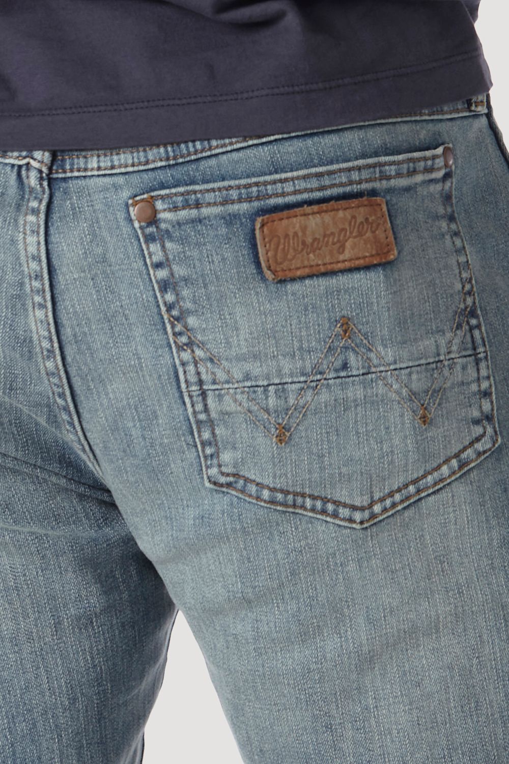 Close-up of the back pocket of light-wash blue denim jeans, showing a brown leather patch with the Wrangler logo and contrast stitching.
