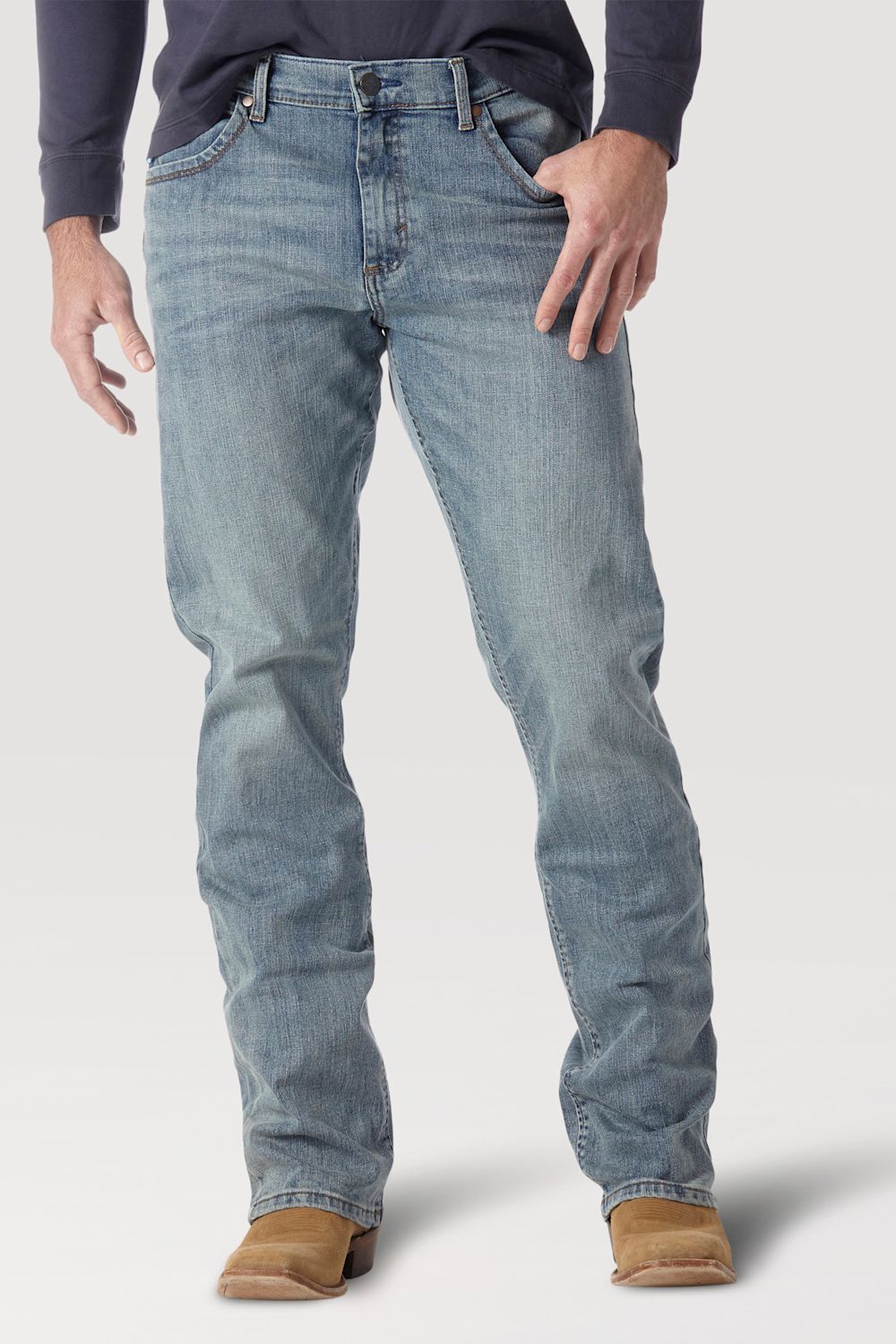 A person wearing light-wash blue denim jeans with a dark navy long-sleeve shirt and tan boots, shown from the waist down against a light gray studio background.