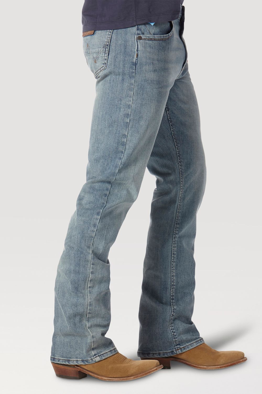 A person shown from the waist down wearing light-wash blue flared jeans and tan cowboy boots against a plain light gray studio background.