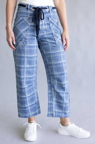 Front view of a model wearing blue plaid cropped wide-leg pants with oversized patch pockets and a navy drawstring waist, paired with a white top and white lace-up sneakers against a neutral gray background.