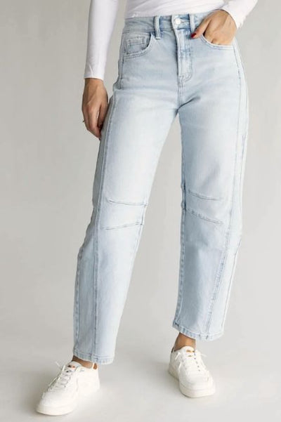Woman wearing light wash barrel leg jeans, a basic white long sleeve top, and white sneakers on a basic studio background