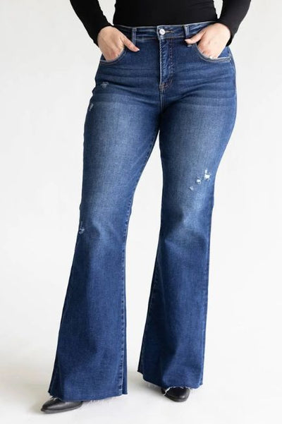 Woman wearing dark wash flare denim jeans, a basic black long sleeve top, and black shoes on a basic studio background