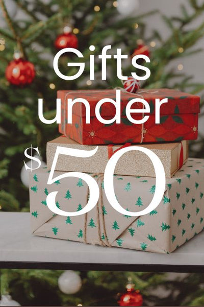 Stack of Christmas gifts with text 'Gifts under $50' in front of a decorated tree.
