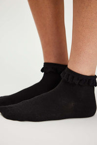 Black ruffled socks worn by a person on a light gray background