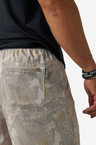 Close-up of a person wearing camouflage athletic shorts with a zippered back pocket, paired with a dark t-shirt and a black wristband.