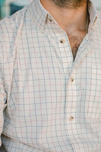 Close-up of a man wearing a white button-down shirt with a subtle blue and pink windowpane plaid pattern.