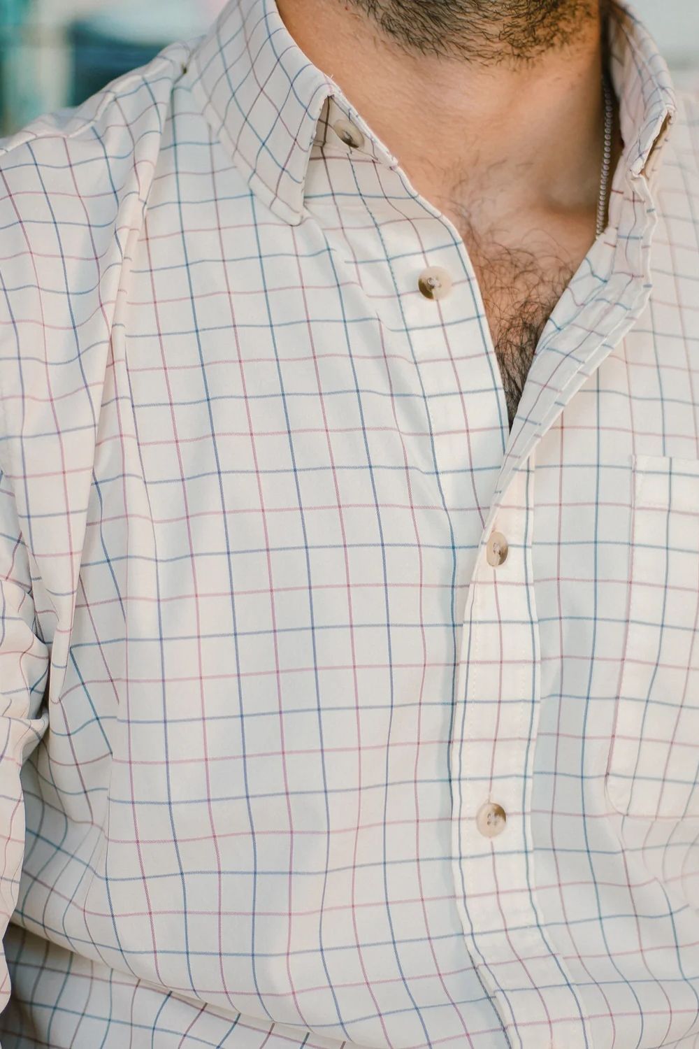 Close-up of a man wearing a white button-down shirt with a subtle blue and pink windowpane plaid pattern.