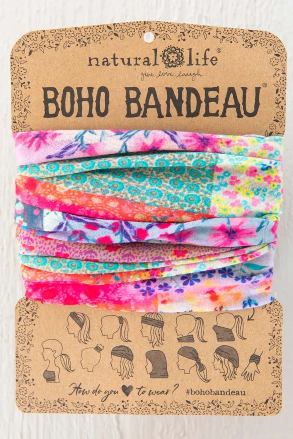 Natural Life Boho Bandeau headwrap in a multicolor floral and patterned fabric, packaged on a brown kraft paper card with instructions on how to wear it.
