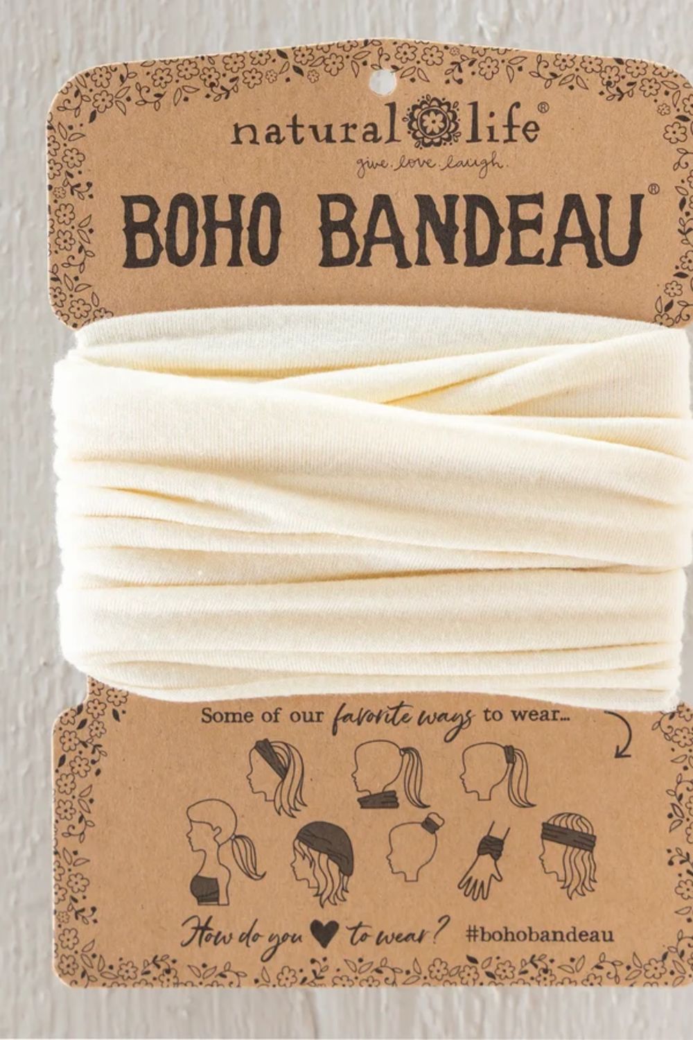 A cream-colored fabric headband wrapped in its original brown kraft paper packaging card, labeled 'natural life BOHO BANDEAU'.