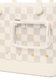 Close-up of a tote bag with a cream and light gray checkerboard pattern, small gold polka dots, and a clear zippered pouch attached on the front.