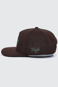 A dark brown flat-brim cap with perforated side panels, featuring a green embroidered 'Waggle' logo on the front and a green graphic on the side, shown against a light gray background.