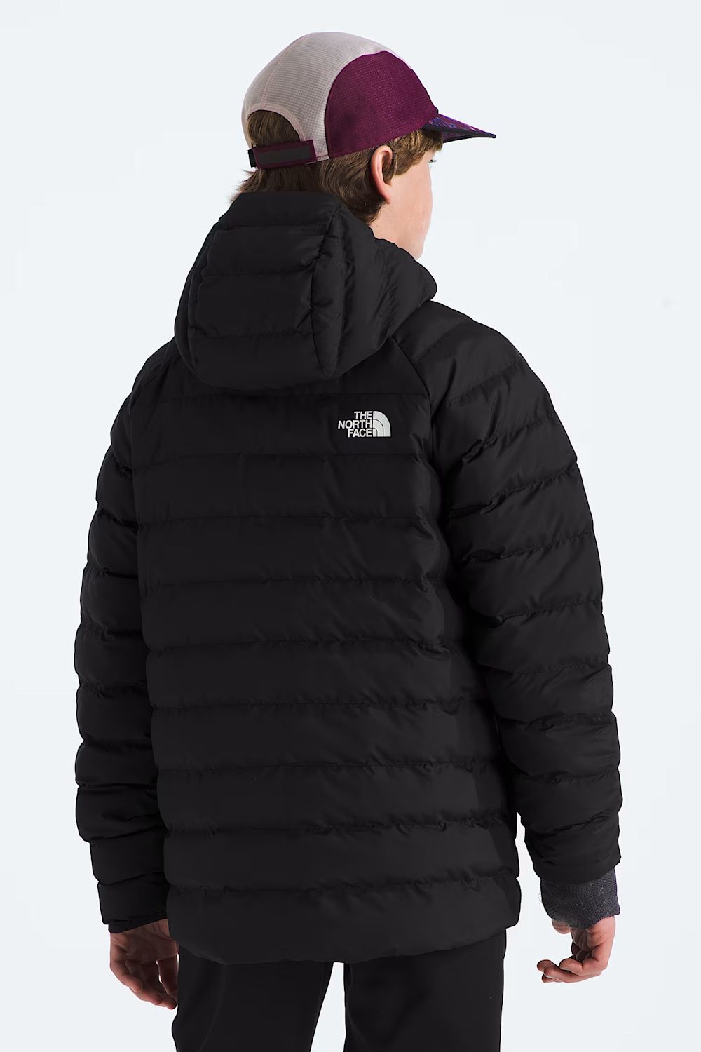 A child shown from the back wearing a black puffer jacket with a white The North Face logo on the upper back, paired with a maroon and gray trucker cap, against a light gray studio background.