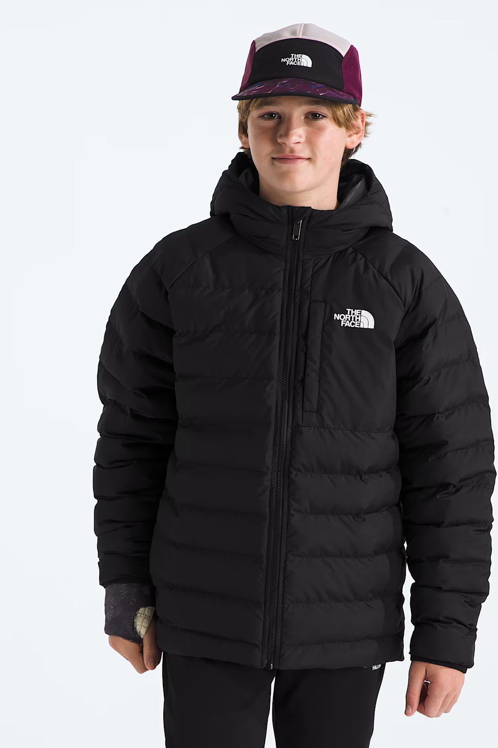 A young man wearing a black puffer jacket with a white The North Face logo on the chest, paired with a black and purple trucker hat, against a plain white background.