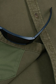 Close-up of olive green fabric with a pocket and button, featuring a pair of dark sunglasses resting on the surface.