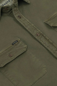 Close-up of an olive green button-up shirt by Poncho, showing the chest pocket, button closure, and inner neck label.