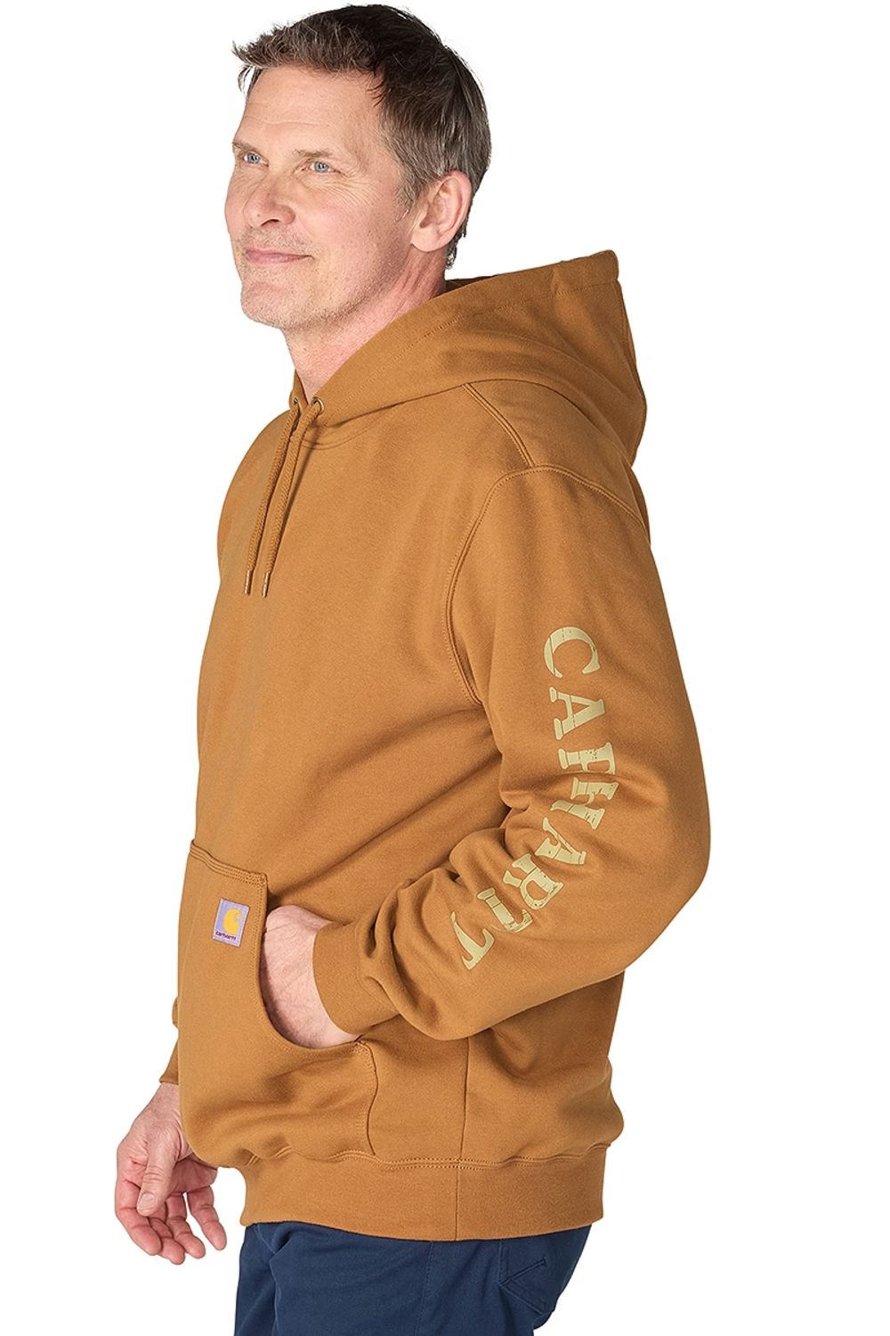 A man wearing a brown Carhartt hoodie and blue jeans stands