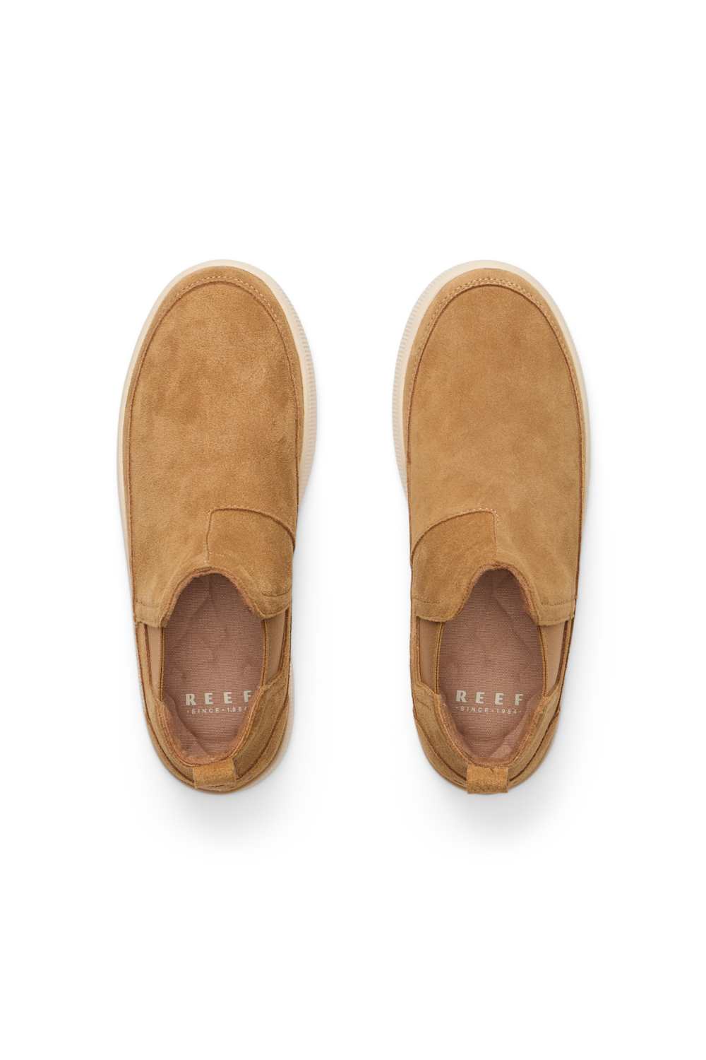 A pair of tan suede slip-on sneakers shown from a top-down view on a white background. The brand name 'REEF' is printed in white on the insole.