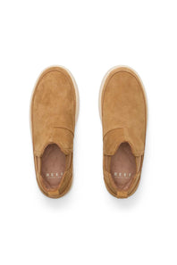 A pair of tan suede slip-on sneakers shown from a top-down view on a white background. The brand name 'REEF' is printed in white on the insole.