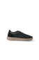 A single low-top sneaker shown from the side profile against a solid white background. The upper is made of black suede, with a thick tan/beige rubber sole.