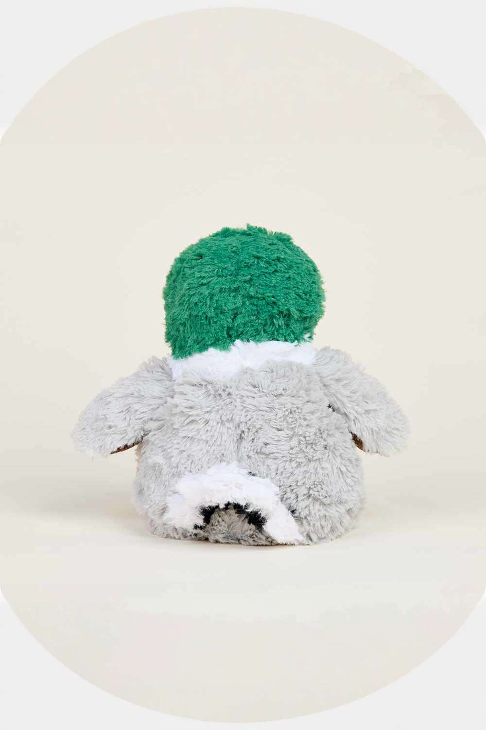 A plush stuffed toy shaped like a duck, shown from the back. It has a bright green fluffy hat, a light gray body, and white accents on the neck and lower back, set against a warm cream-colored background with a circular vignette.