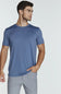 A man wearing a slate blue short-sleeve crewneck t-shirt and light gray trousers, standing against a light gray studio background.