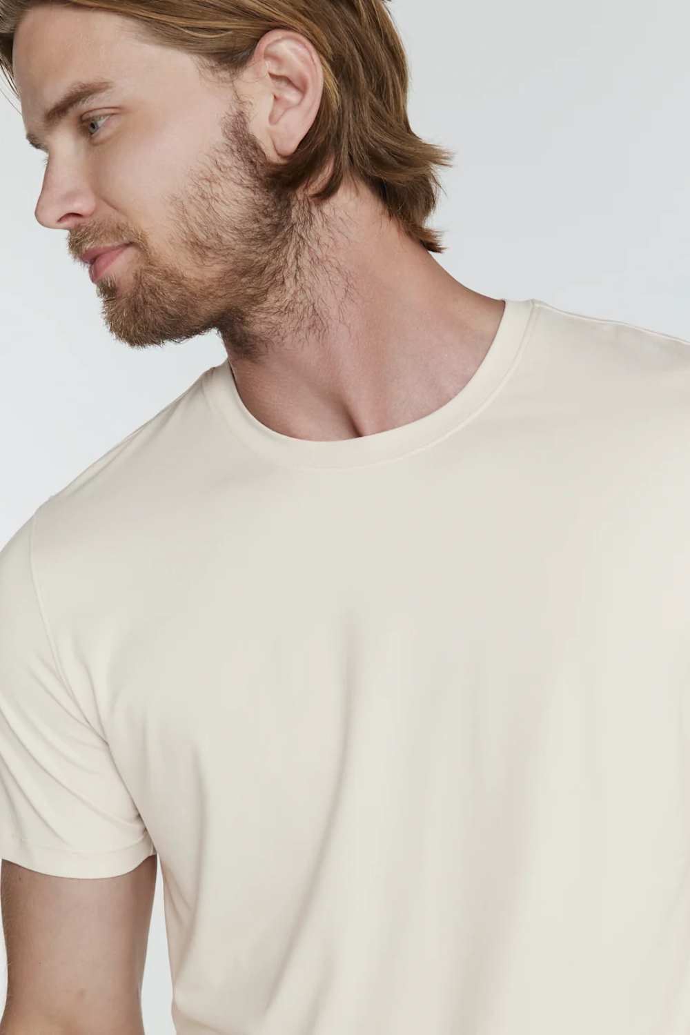A close-up of a man wearing a plain cream-colored crew-neck t-shirt against a light gray background.