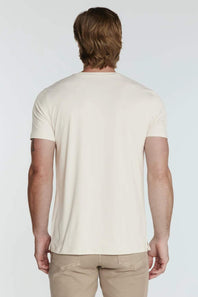 A man viewed from behind wearing a plain cream-colored short-sleeve t-shirt and khaki pants, set against a light gray studio background.