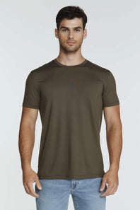 A man wearing a short-sleeve crewneck t-shirt in olive brown, paired with light blue jeans, standing against a light gray studio background.
