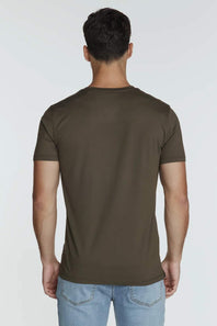 A man viewed from the back wearing a solid dark olive brown short-sleeve t-shirt and light blue jeans, set against a plain light gray studio background.