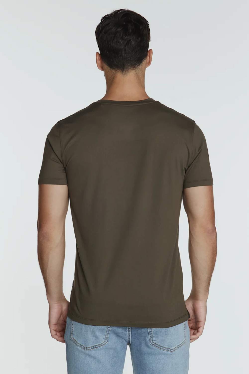 A man viewed from the back wearing a solid dark olive brown short-sleeve t-shirt and light blue jeans, set against a plain light gray studio background.