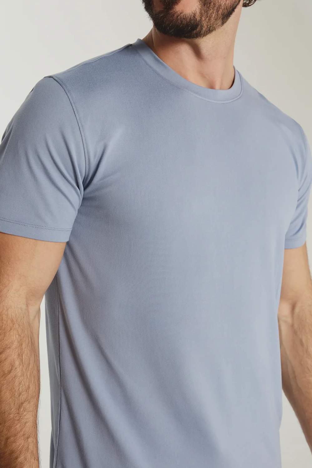 A close-up of a man wearing a light blue crew-neck t-shirt against a neutral beige background.