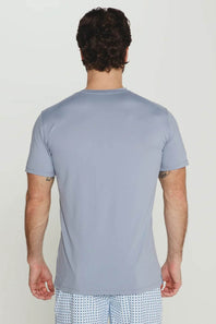 A man viewed from behind wearing a light blue-gray crewneck t-shirt and patterned shorts against a plain light background.