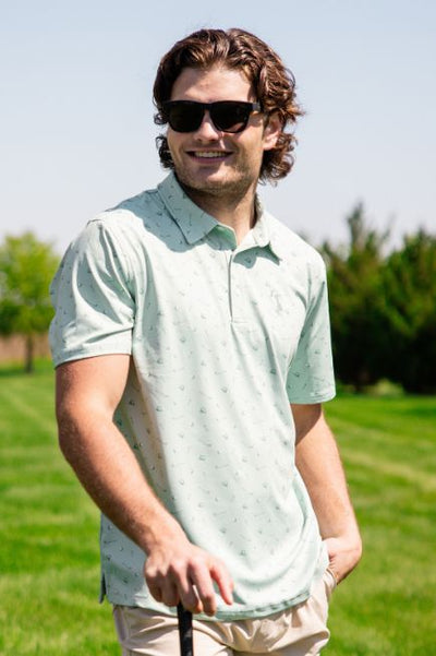 Man wearing a green with small golf print designs polo and black sunglasses on a golf course