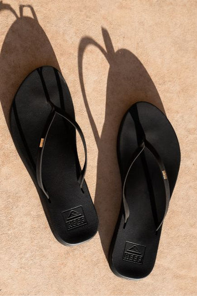 Black skinny strap thong style flip-flops on a tan gradient style floor