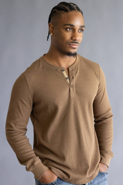 Image of a man man wearing a brown textured shirt and jeans, standing against a grey background.