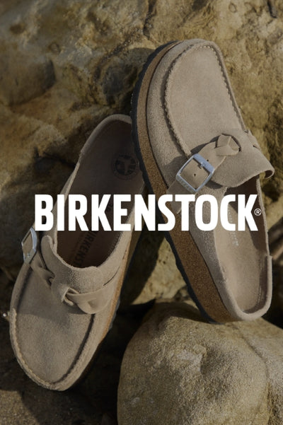 A pair of taupe Birkenstock shoes on sand with a dark image overlay with BIRKENSTOCK text