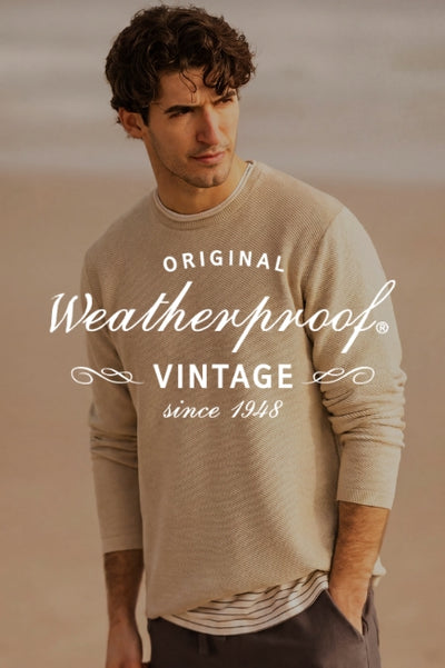 A man outdoors wearing a tan sweater with a dark overlay with text ORIGINAL Weatherproof VINTAGE since 1948