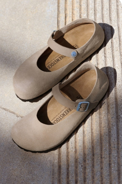 A pair of Birkenstock Mary Jane like shoes on a beige sidewalk