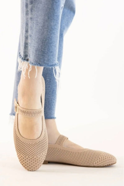 A woman wearing beige Mary Jane style shoes wearing jeans on a white background